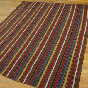 Flatwoven rug displays vertical stripes of maroon, blue, yellow, and black on a textured wood floor.