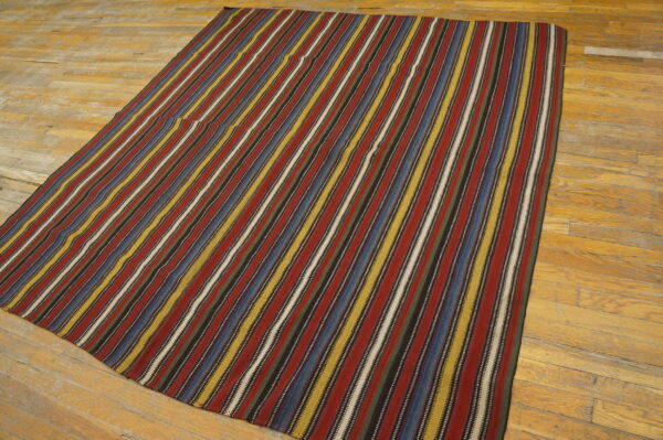 Flatwoven rug displays vertical stripes of maroon, blue, yellow, and black on a textured wood floor.