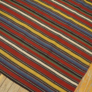 Multicolored striped rug featuring red, yellow, blue, green, and cream bands on distressed wood.