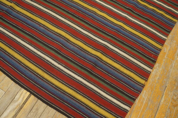 Multicolored striped rug featuring red, yellow, blue, green, and cream bands on distressed wood.