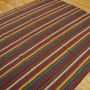 Low-pile rug with wide stripes in red, blue, yellow, and white on a rustic wood floor.