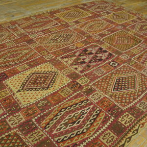 Geometric flatweave rug with repeating diamond panels in reds, olives, oranges, and cream on rustic wood floors.
