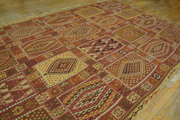 Geometric flatweave rug with repeating diamond panels in reds, olives, oranges, and cream on rustic wood floors.