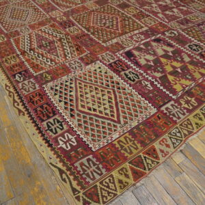 Geometric flatweave rug in red, burgundy, yellow, and brown tones covering rustic wood plank flooring.