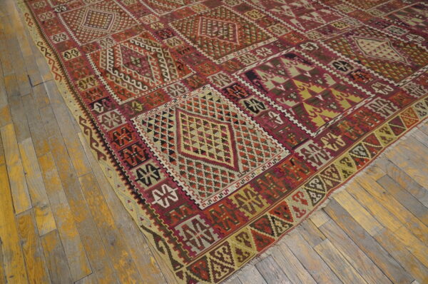 Geometric flatweave rug in red, burgundy, yellow, and brown tones covering rustic wood plank flooring.