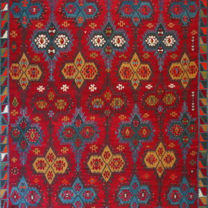A low-pile red rug with repeating geometric patterns in blue, gold, dark gray, and white.