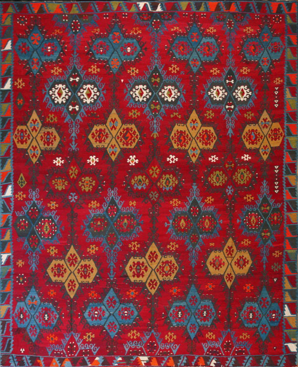 A low-pile red rug with repeating geometric patterns in blue, gold, dark gray, and white.