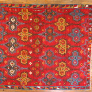 Flat-woven red rug featuring complex blue, mustard, and white geometric medallion patterns on a rustic wood floor.