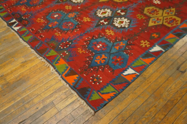Red rug featuring vibrant geometric medallions and zigzag borders on wide plank wooden flooring.