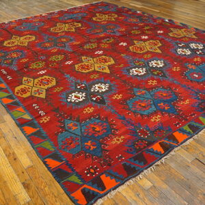 Red flatweave rug featuring colorful blue, gold, green, and orange geometric patterns on hardwood flooring.