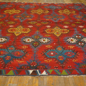 Geometric flatweave rug featuring red, blue, and yellow tribal patterns rests on light brown hardwood flooring.