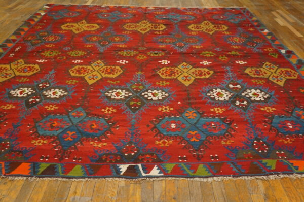 Geometric flatweave rug featuring red, blue, and yellow tribal patterns rests on light brown hardwood flooring.