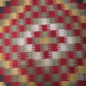 Flat-weave rug with interlocking notched blocks in red, olive, mustard, white, and black.