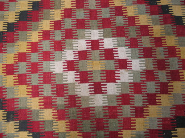 Flat-weave rug with interlocking notched blocks in red, olive, mustard, white, and black.