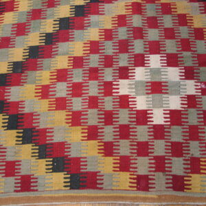 Geometric flatweave rug featuring interlocking sawtooth stripes in red, yellow, gray, black, and cream colors.