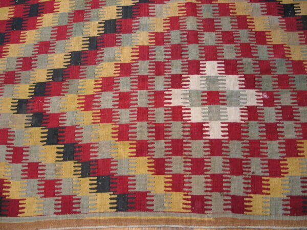 Geometric flatweave rug featuring interlocking sawtooth stripes in red, yellow, gray, black, and cream colors.