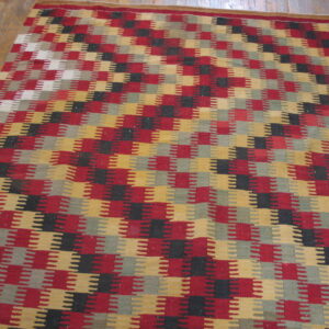 Stepped geometric flatweave rug in red, gold, black, and gray lying partially on a wooden floor.