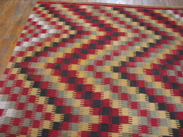 Stepped geometric flatweave rug in red, gold, black, and gray lying partially on a wooden floor.