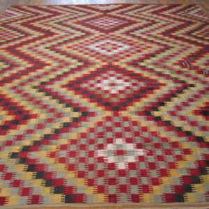 A colorful flatweave rug with stepped red, gold, and gray geometric diamond patterns covers a light wood floor.
