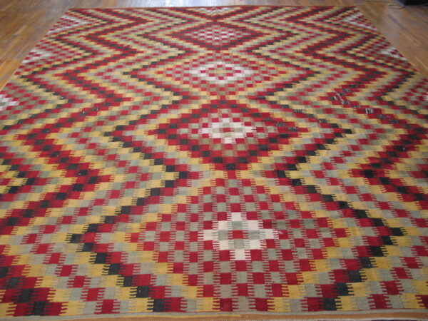 A colorful flatweave rug with stepped red, gold, and gray geometric diamond patterns covers a light wood floor.