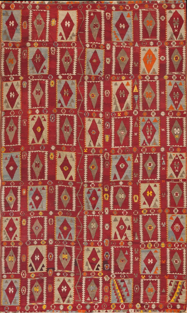 Flatweave rug with a repeating geometric grid pattern of red, gray, blue, and tan diamond motifs.