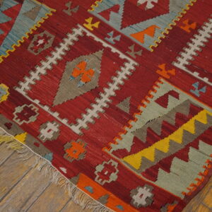 Geometric flatweave rug in red, yellow, teal, and beige patterns resting on distressed wooden planks.
