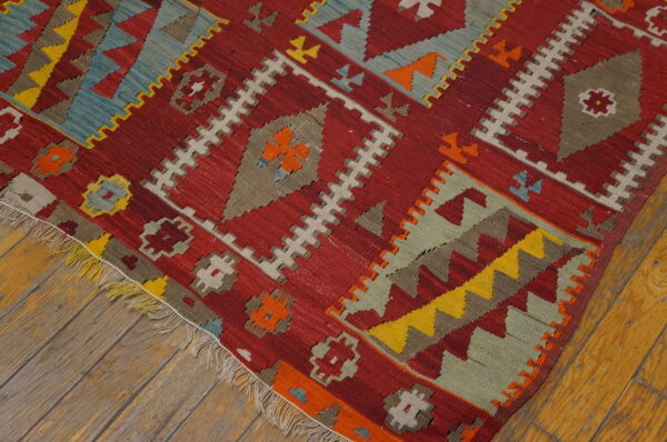 Geometric flatweave rug in red, yellow, teal, and beige patterns resting on distressed wooden planks.