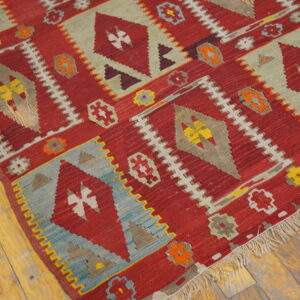 Red geometric flatweave rug with diamond motifs and colorful accents resting on wide plank wood floors.