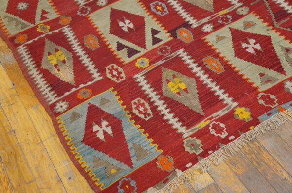 Red geometric flatweave rug with diamond motifs and colorful accents resting on wide plank wood floors.