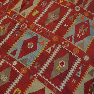 Geometric flatweave rug featuring red, blue, gray, and olive diamond motifs on a wood floor.