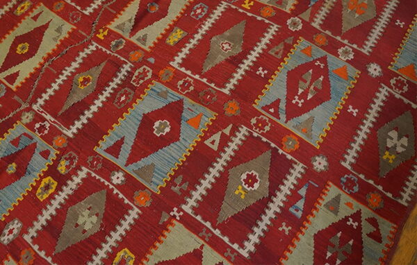 Geometric flatweave rug featuring red, blue, gray, and olive diamond motifs on a wood floor.