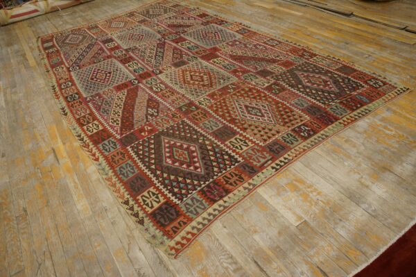 Geometric patchwork rug in red, burgundy, and teal laid diagonally across distressed wooden floorboards.