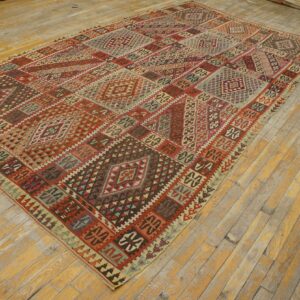 Flatweave rug with segmented geometric patterns in red, brown, and teal on worn hardwood floors.
