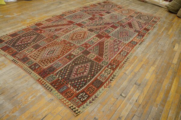 Flatweave rug with segmented geometric patterns in red, brown, and teal on worn hardwood floors.