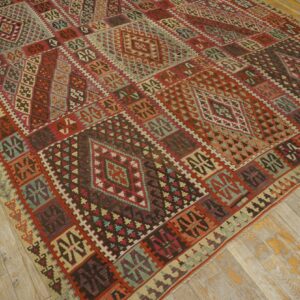 Flat-woven rug featuring a rich geometric pattern in red, teal, and brown colors on distressed wood planks.