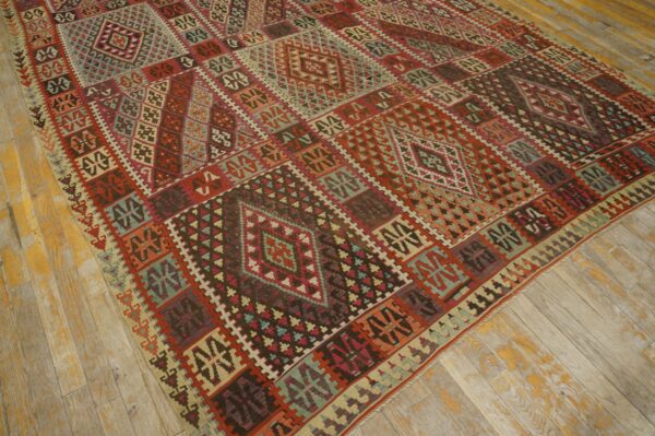 Flat-woven rug featuring a rich geometric pattern in red, teal, and brown colors on distressed wood planks.