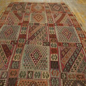 Complex geometric rug in shades of red, teal, brown, and pink covering wide, distressed wood plank flooring.