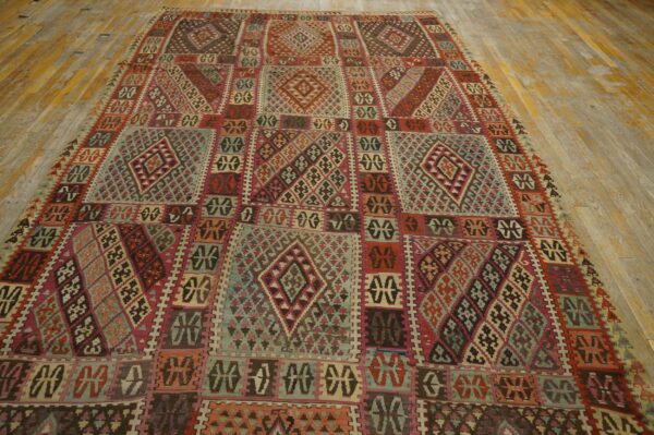 Complex geometric rug in shades of red, teal, brown, and pink covering wide, distressed wood plank flooring.