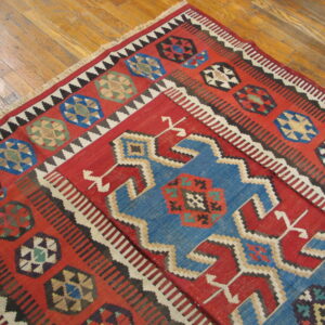 Geometric flatweave rug in red, blue, black, and white covers an old, honey-toned wood floor.