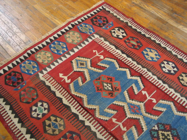 Geometric flatweave rug in red, blue, black, and white covers an old, honey-toned wood floor.