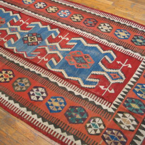 Red and blue flat-weave rug with bold geometric patterns and stepped medallions on wood floor.
