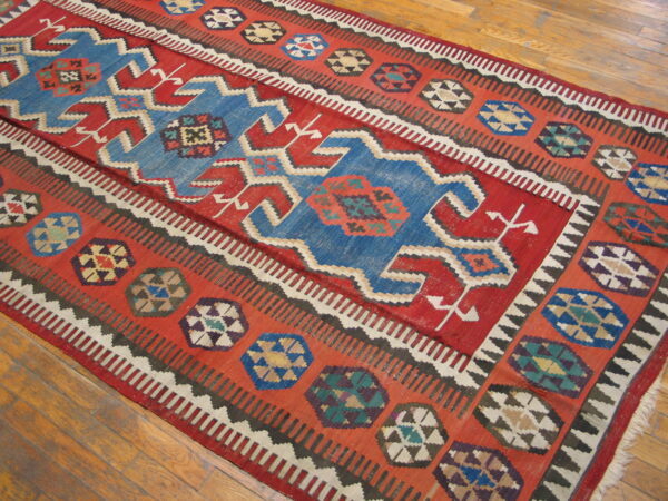 Red and blue flat-weave rug with bold geometric patterns and stepped medallions on wood floor.
