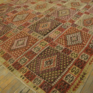 Geometric flatweave rug featuring red, brown, and tan diamonds covers distressed wooden floorboards.