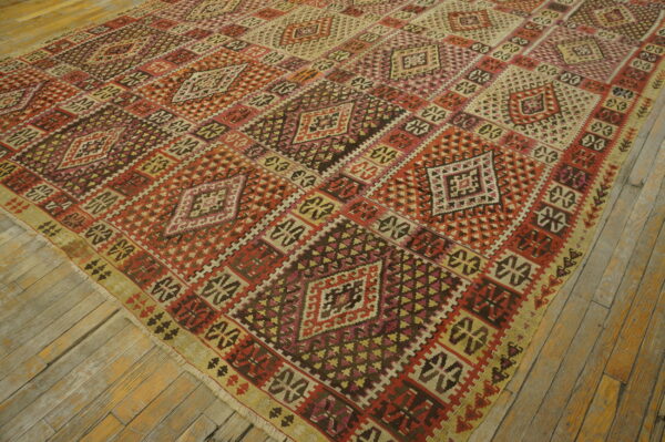 Geometric flatweave rug featuring red, brown, and tan diamonds covers distressed wooden floorboards.