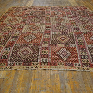 Flatweave rug with repeating red, beige, and dark geometric diamond panels on rustic wood planks.