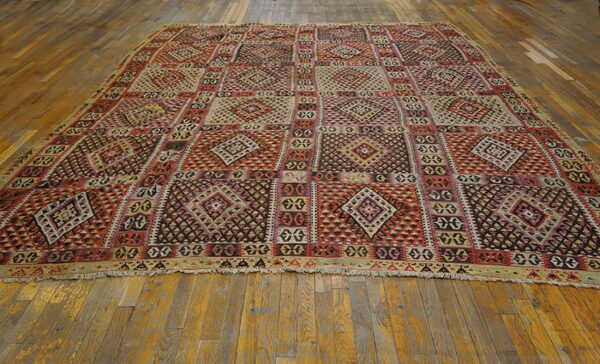 Flatweave rug with repeating red, beige, and dark geometric diamond panels on rustic wood planks.