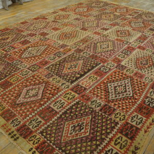 Large geometric rug in reds, browns, and cream hues on light natural wood plank flooring.