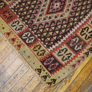 Flatweave rug with pink, red, brown, and khaki geometric patterns rests on worn wooden floorboards.