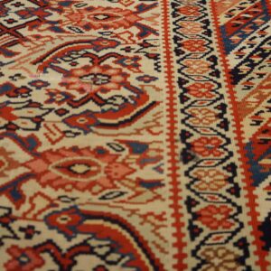 Low-pile rug detail featuring ivory ground with complex geometric designs in red and navy blue.