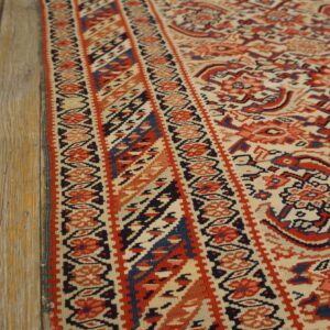 The rug's detailed red and blue geometric pattern is seen next to distressed light wood flooring.
